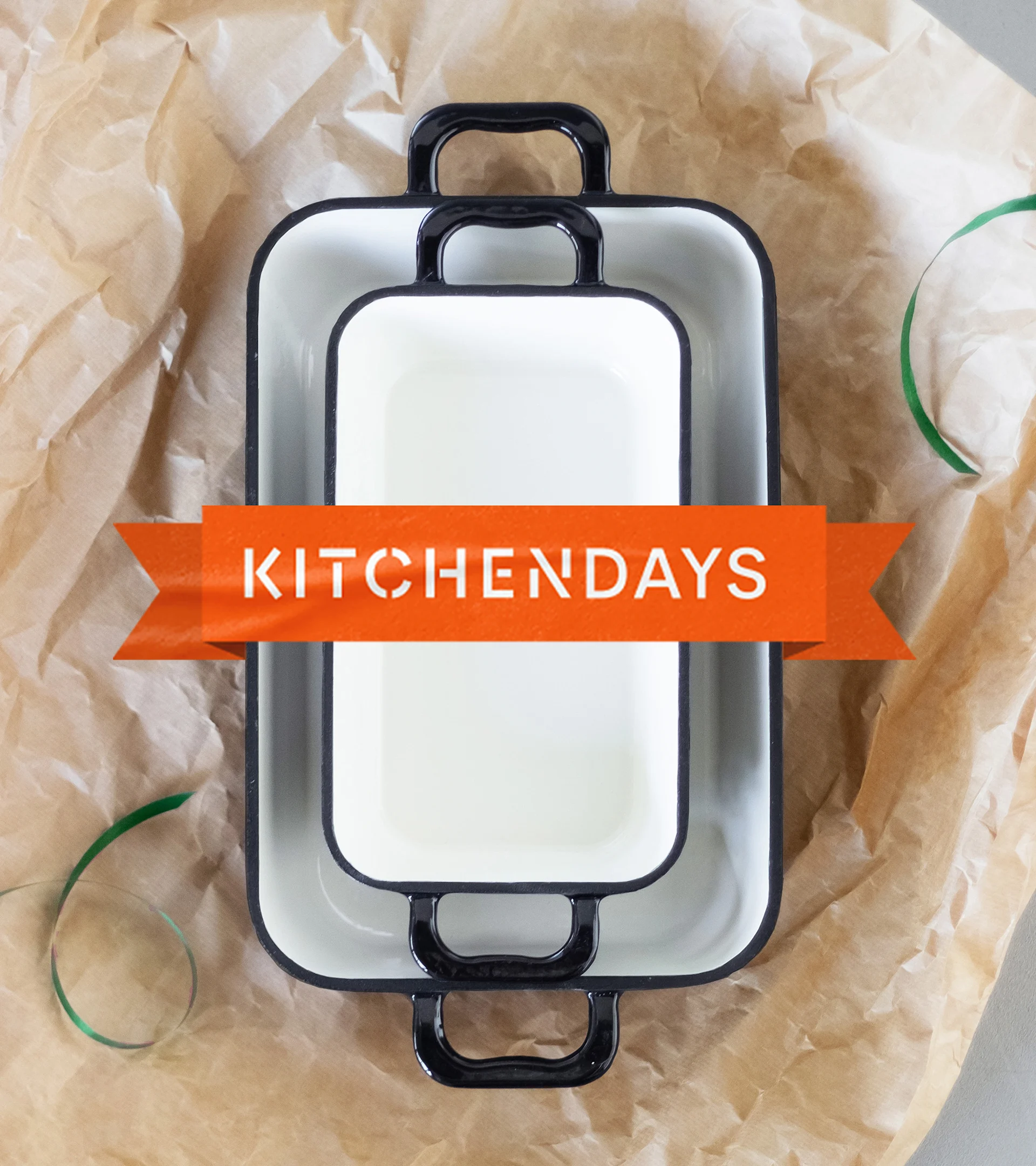 Two nested white rectangular baking dishes with black rims and handles, on crumpled brown paper, with an orange banner saying 'KITCHENDAYS'.