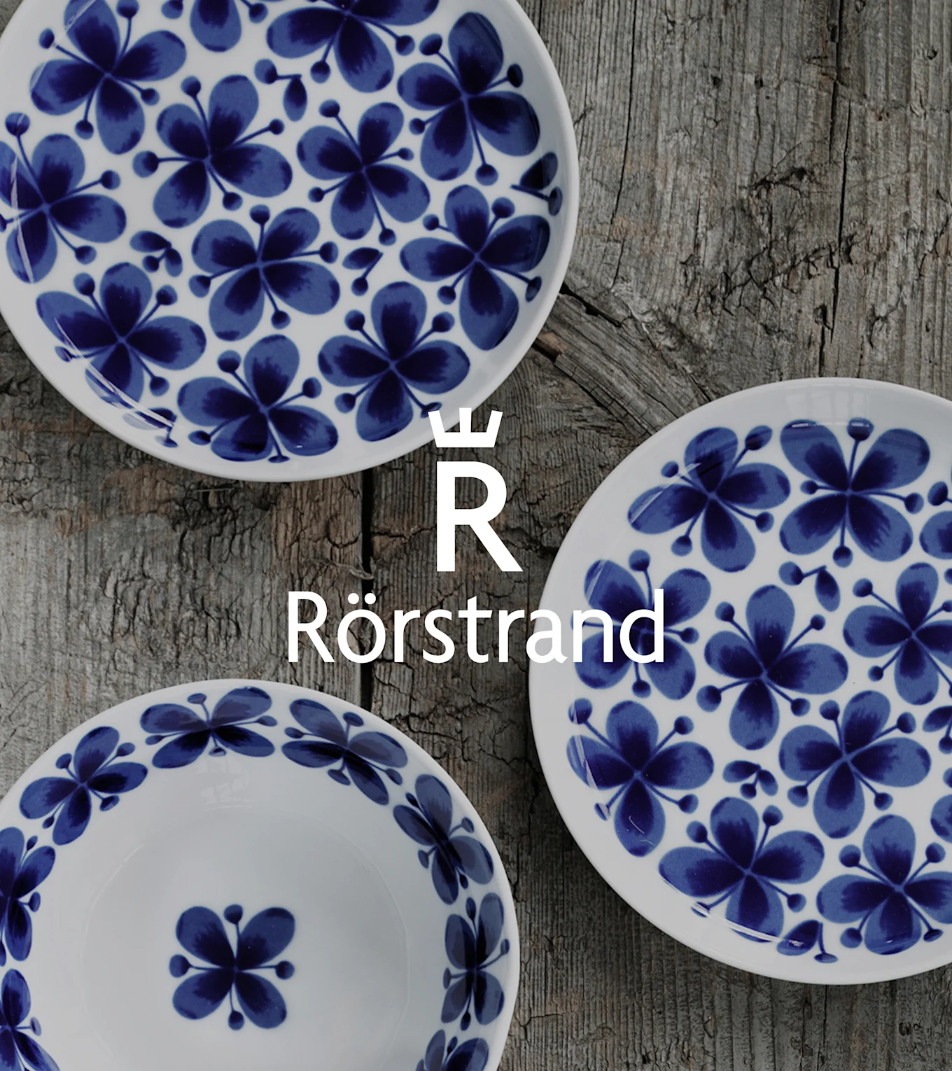 Three white plates with blue floral patterns, arranged on a weathered wooden table. Rörstrand logo overlaid.