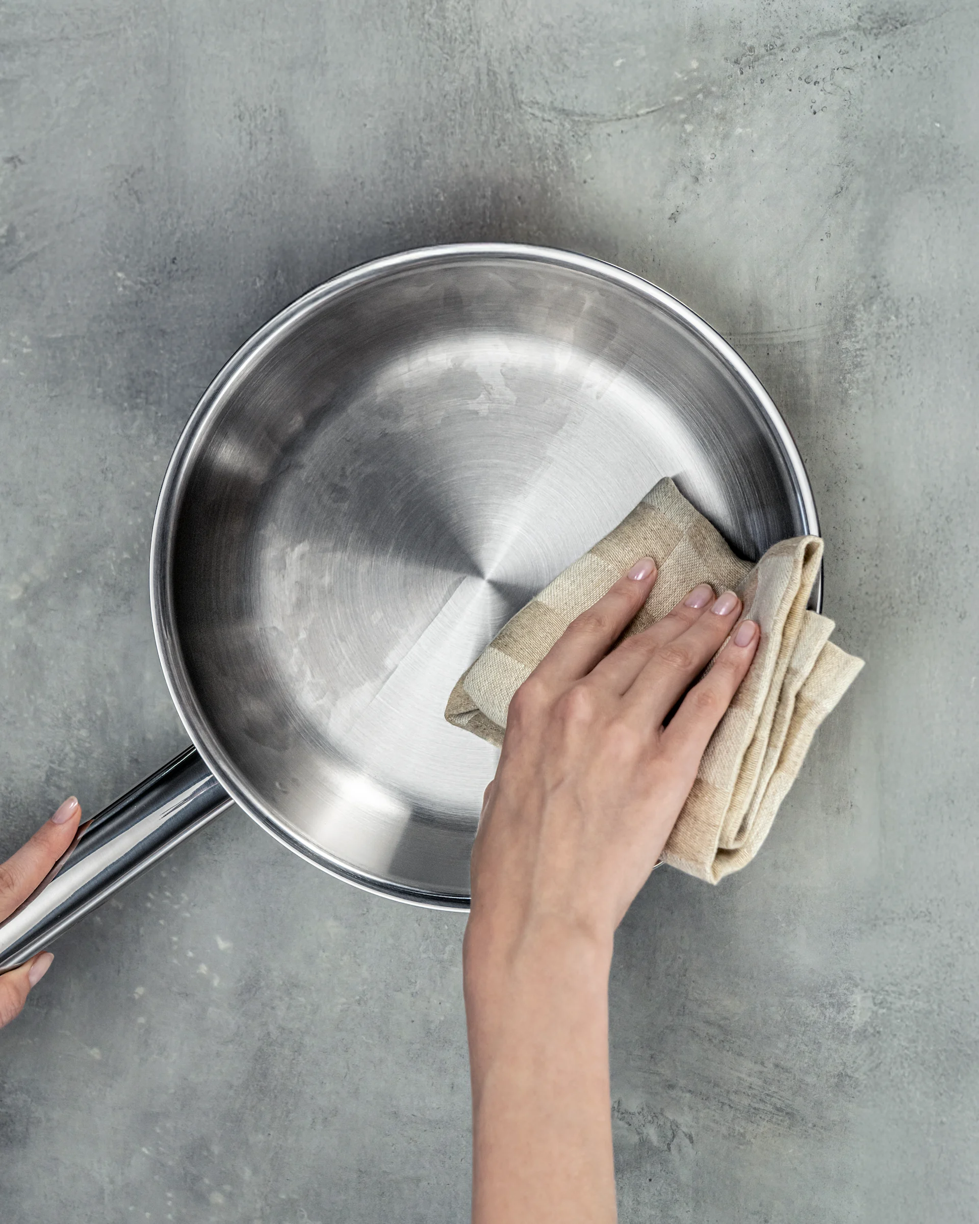 Close-up of a hand cleaning a stainless steel pan with a beige cloth.