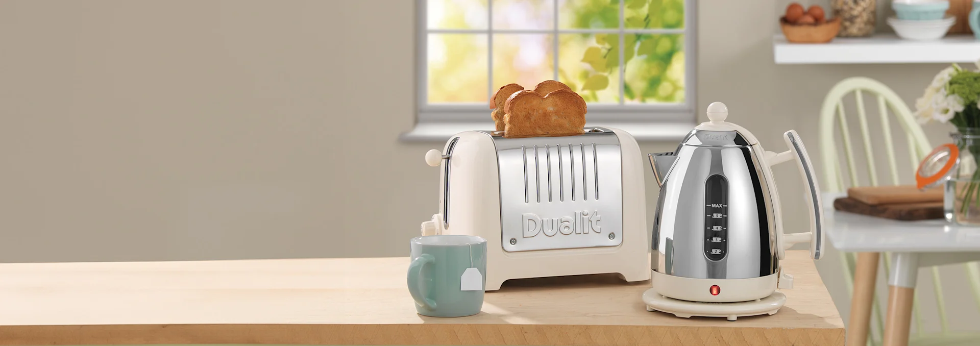 A beige and chrome toaster with two slices of toast and a matching kettle sit on a wooden counter with a mug of tea.