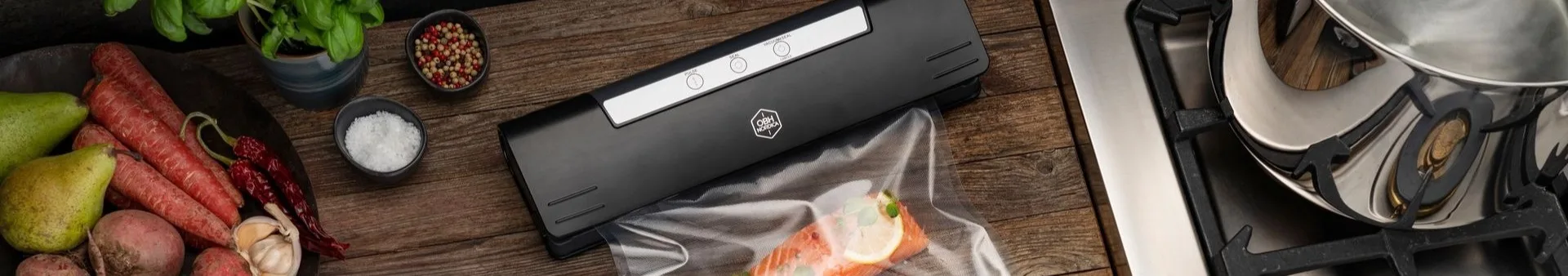 Black vacuum sealer processing salmon, surrounded by fresh vegetables, herbs, and spices on a wooden counter.