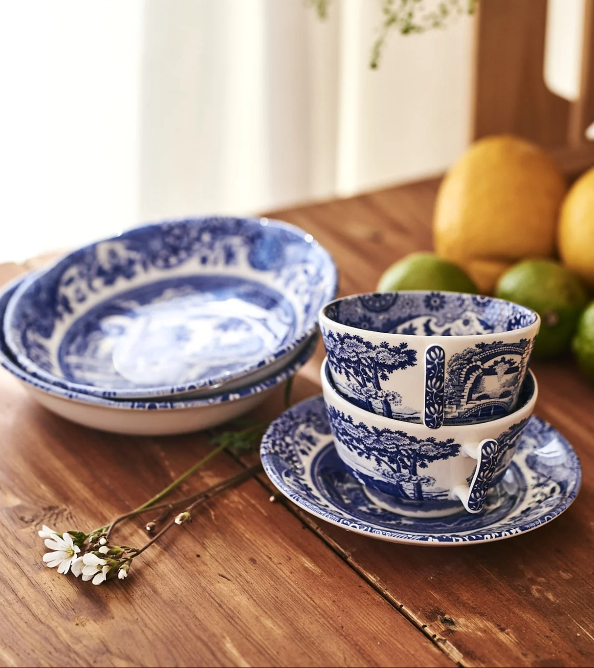 Blue and white patterned ceramic dinnerware, including bowls, teacups, and saucers, on a wooden table.
