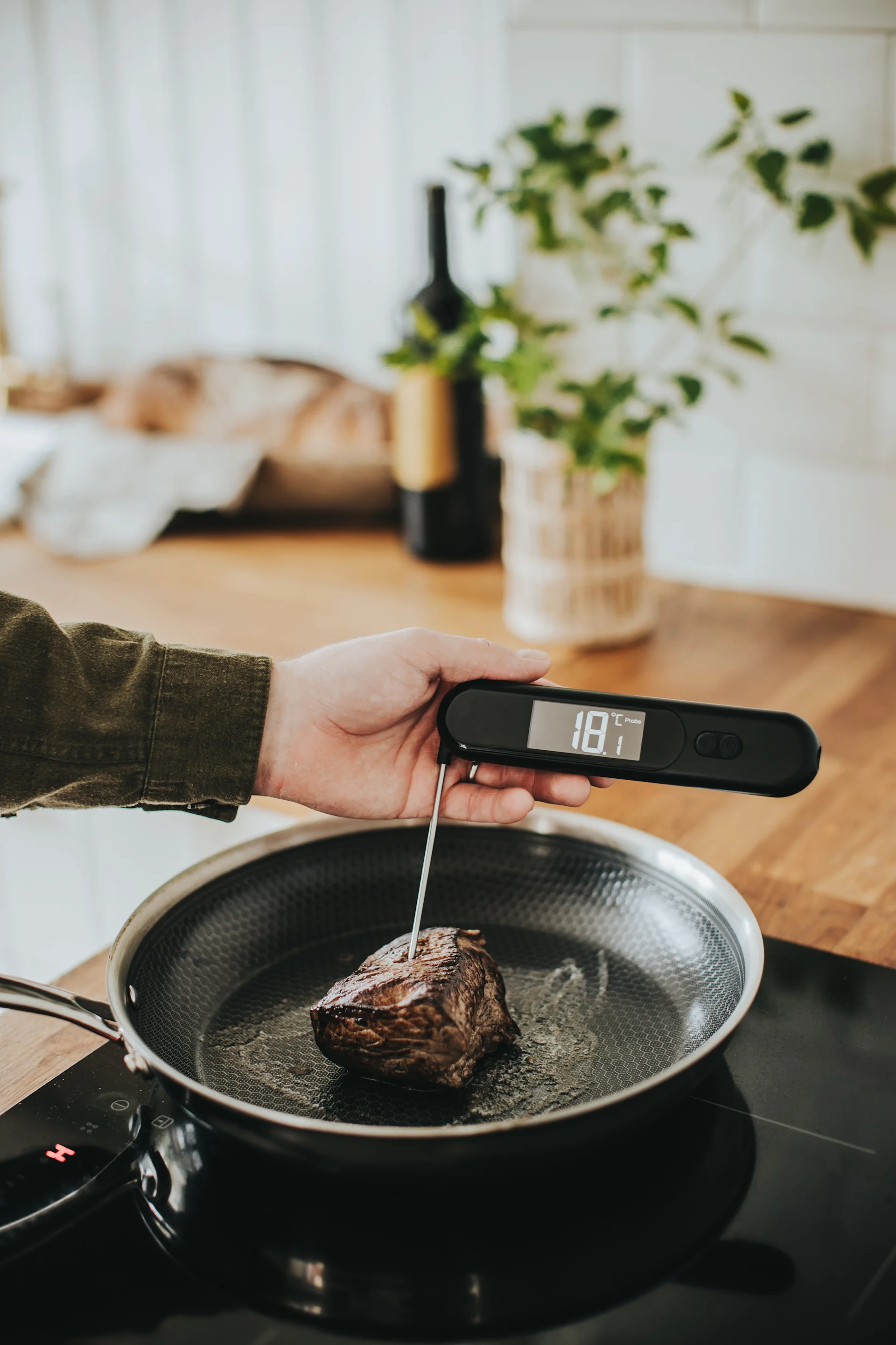 Hand checking meat temperature with a digital thermometer in a frying pan.
