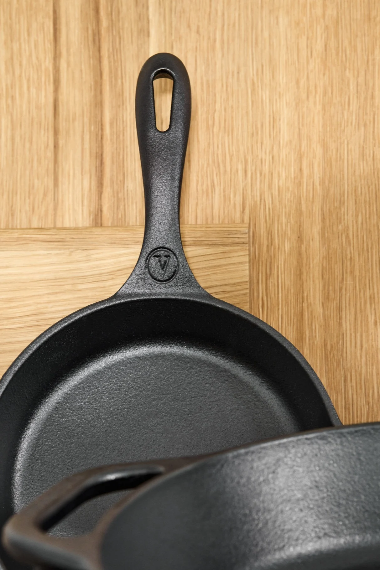 Two black cast iron frying pans with a logo on one handle, on a wooden surface.