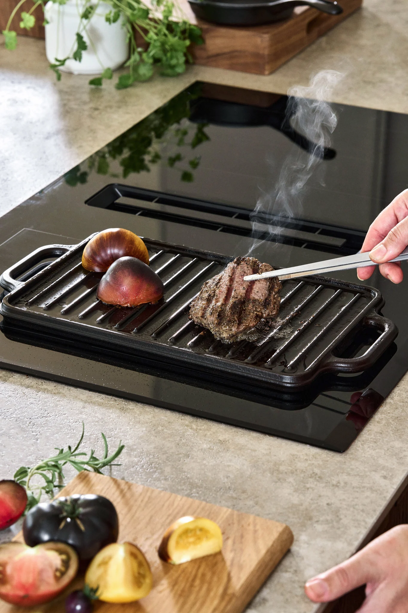 A cast iron frying plate on an induction hob with a couple of tomatoes and a piece of steak. 