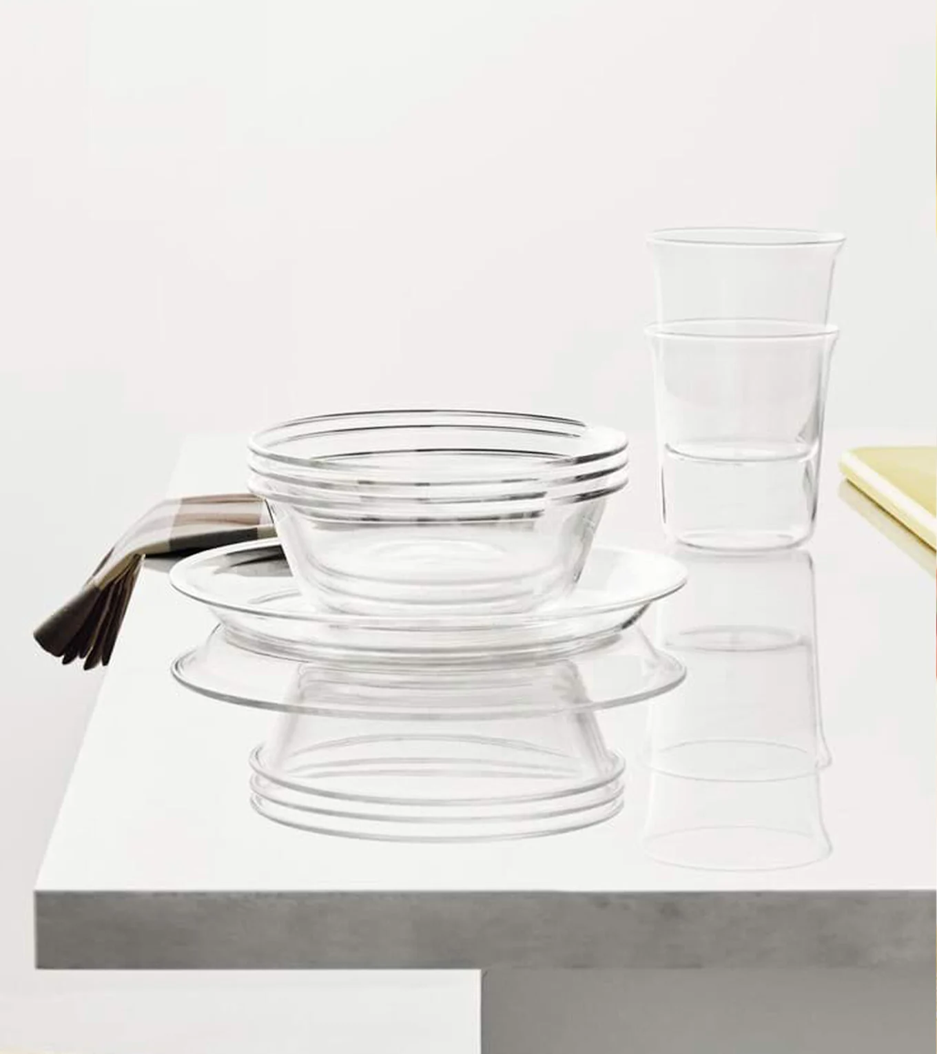Clear glass bowls, plates, and tumblers stacked on a white surface with a striped napkin.