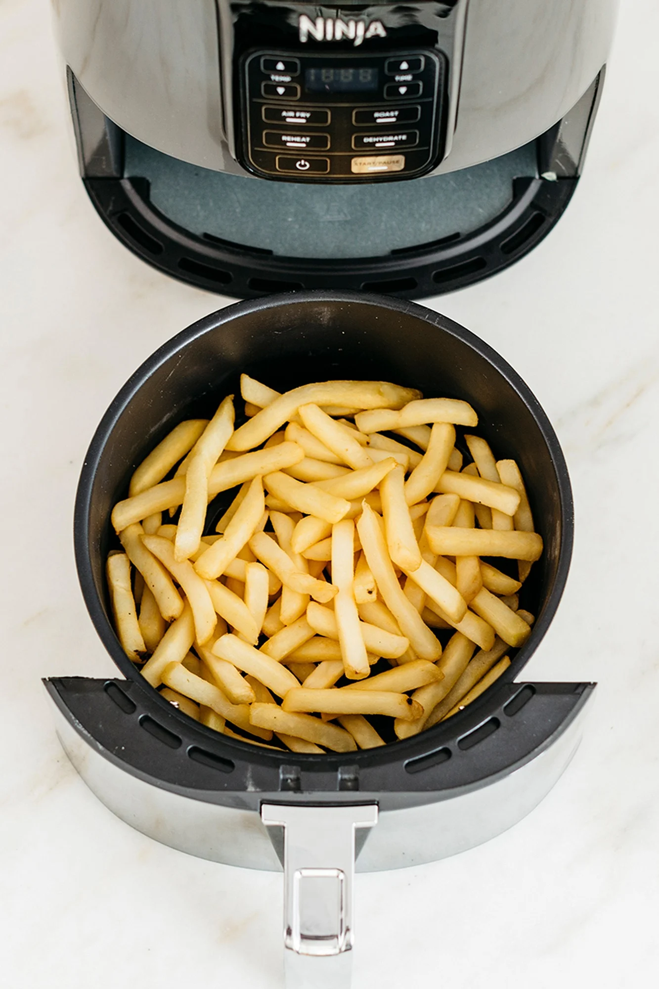 An air fryer basket filled with golden french fries, with the top part of a black air fryer visible above it.