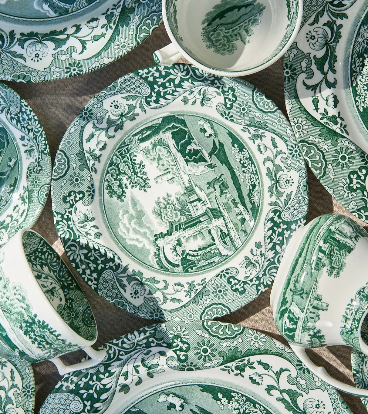 Overhead view of various green and white patterned ceramic plates and cups with intricate landscape and floral designs.