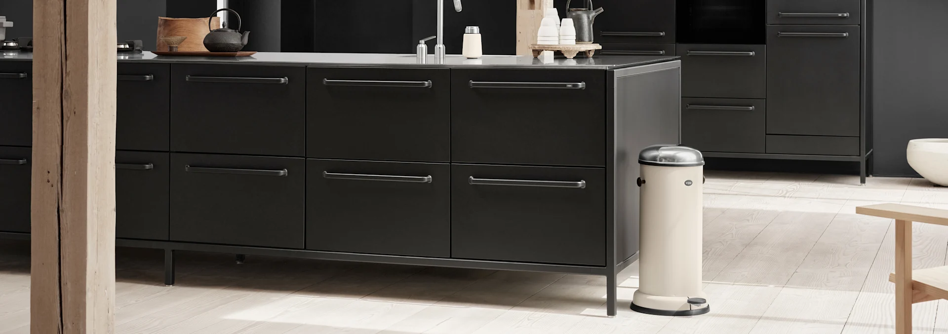 A modern kitchen with dark grey cabinets, a sink, and a beige pedal bin on a light wooden floor.