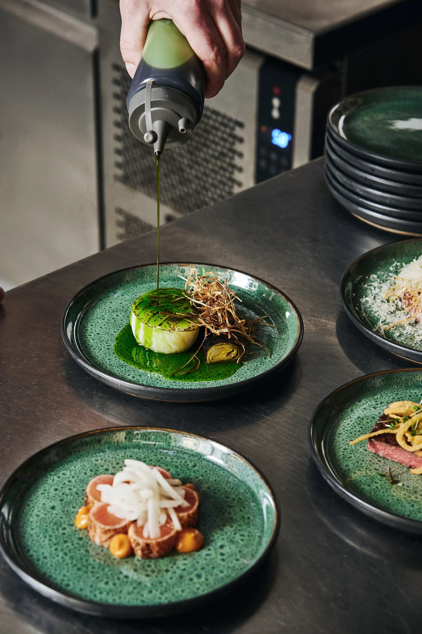 The right tools will allow you to plate like a professional. Here you see the Plate it squeeze bottle for garnishing, with green oil, being poured over a plate of food.