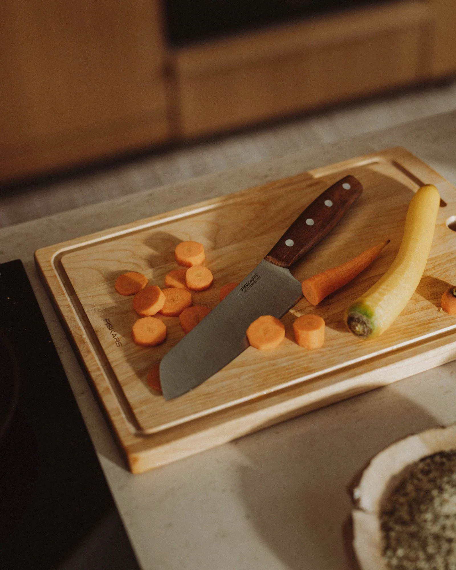 A wooden cutting board with sliced orange carrots, a whole yellow carrot, and a knife with a wooden handle.