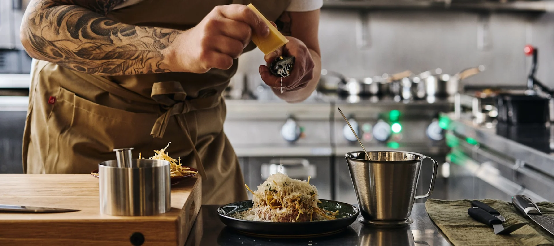 Discover how to plate like a professional, here you see a chef grating cheese over a plate of beef tartare inside a professional kitchen.