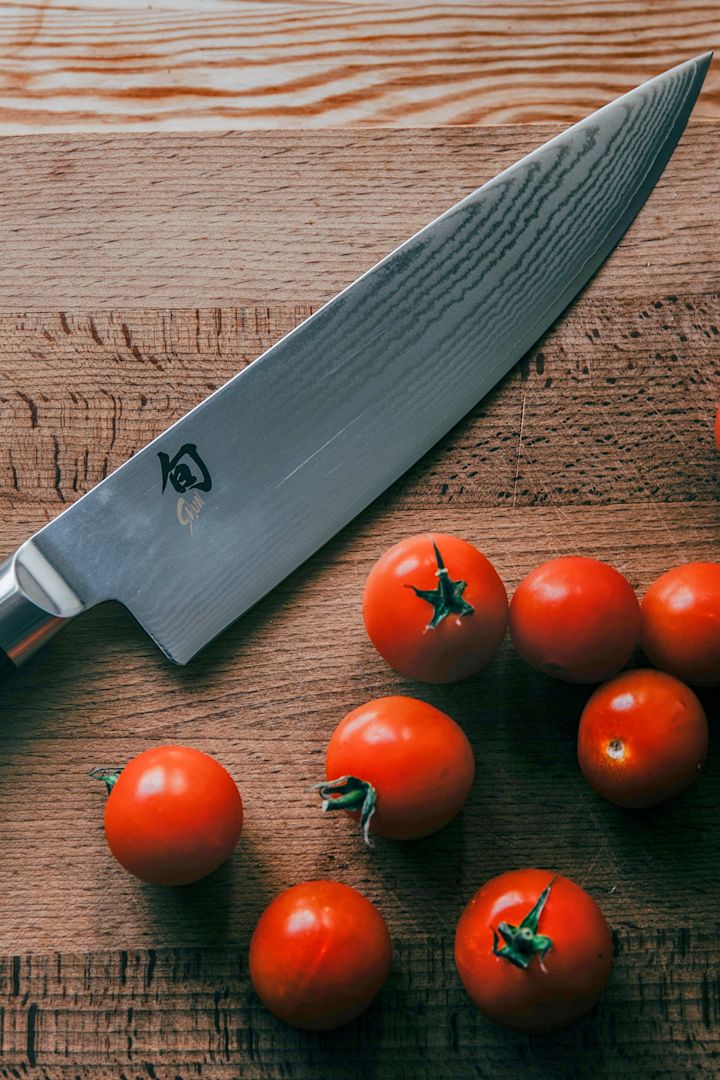 A close up of a Kai Shun Gyuto knife on a wooden chopping board with tomatoes.