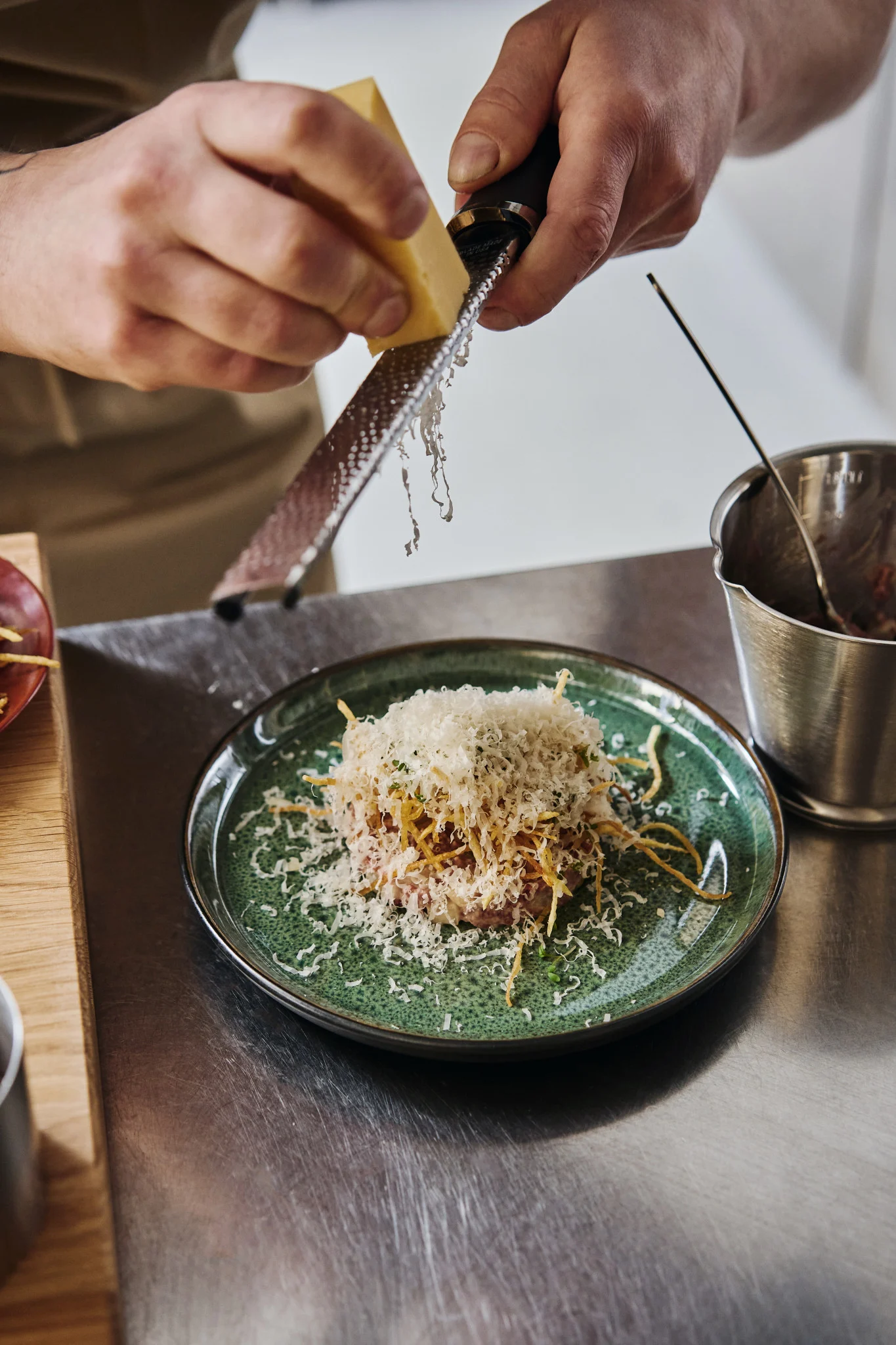 Here you can discover how to plate like a professional, you see a professional chef grating cheese over a green plate of food.