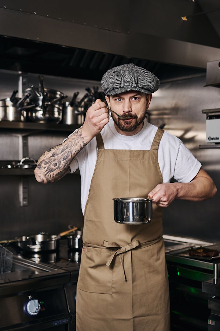 A professional chef spoons sauce over a steak in a stainless steel Nordwik frying pan. 