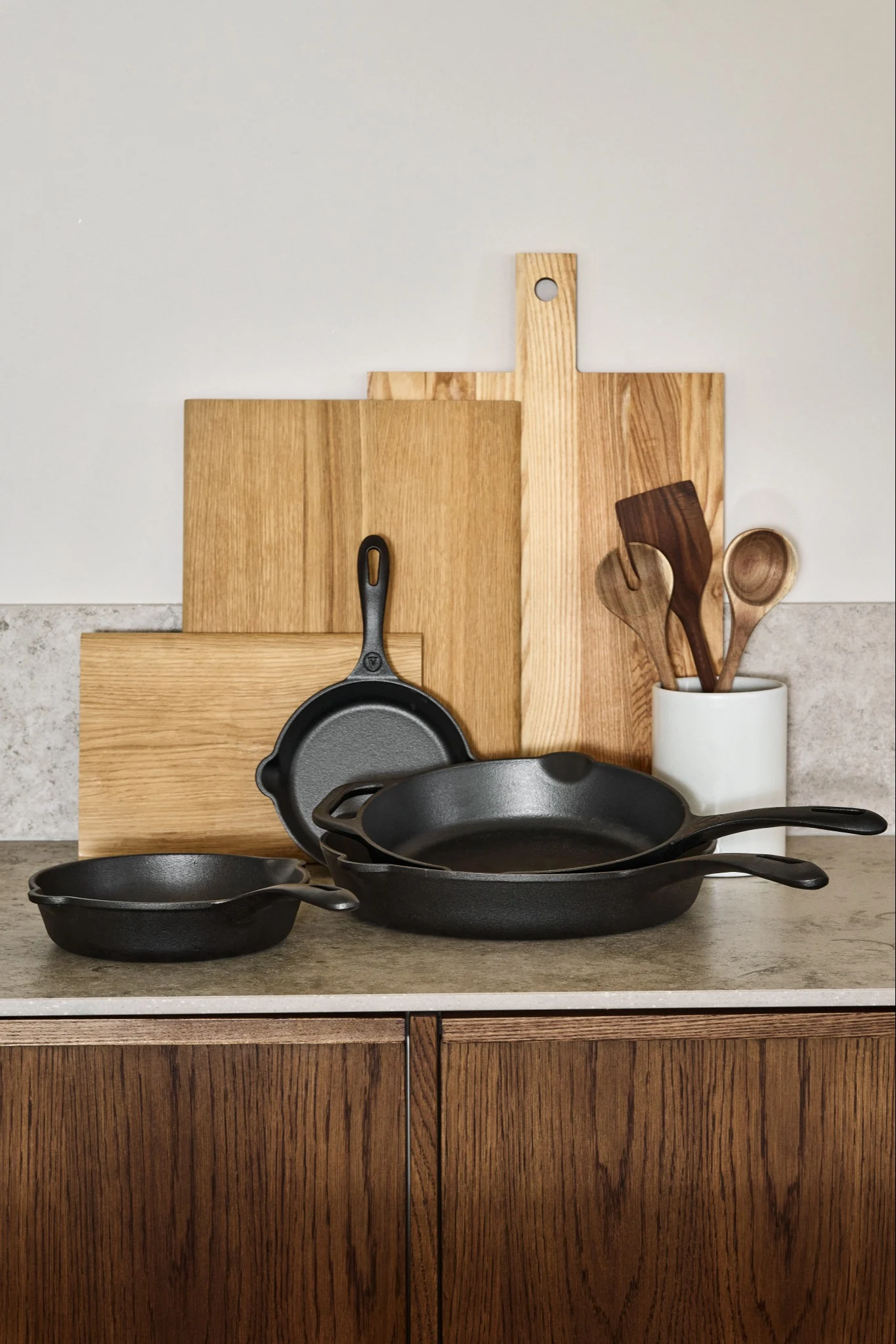 A collection of cast iron pans stacked on a kitchen side with wooden chopping boards placed behind. 